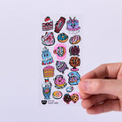 Sheet of colorful cartoon-style stickers held by a hand on a light purple background