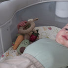 Baby lying in a crib with colorful soft toys