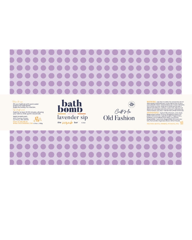 A rectangular package of bath bomb labeled 'lavender sip' with a lavender purple polka dot pattern on a white background. Visible text includes 'bath bomb', 'lavender sip', 'Craft by Old Fashion', and 'The Artisan Bar'.