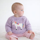 A baby sitting and wearing a light purple knit sweater with a white unicorn design featuring a rainbow mane and tail, paired with pink pants against a soft white background.