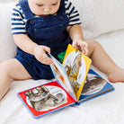 Child reading a colorful book with animal illustrations on a white surface