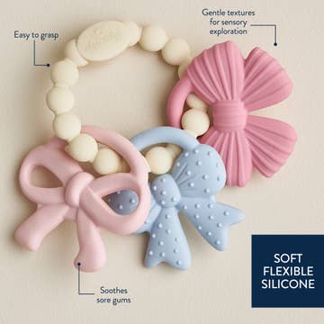 Teething ring with pink and blue bows and white beads on a beige background