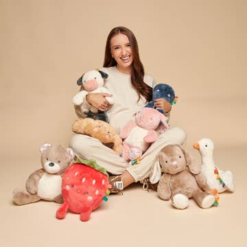 Woman holding and surrounded by various plush toys on a beige background