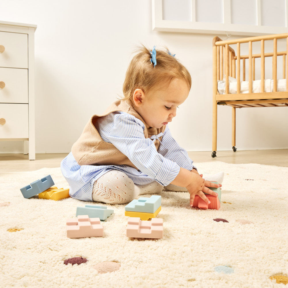 Child playing with colorful blocks on a carpeted floor in a room with furniture.