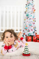 Child in pajamas with a Christmas tree toy and decorated tree in the background