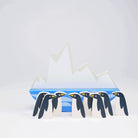 A collection of eight stylized wooden penguins lined up in a row in front of a rocking white iceberg base resting on a blue-and-white wavy ocean design against a clean white background.