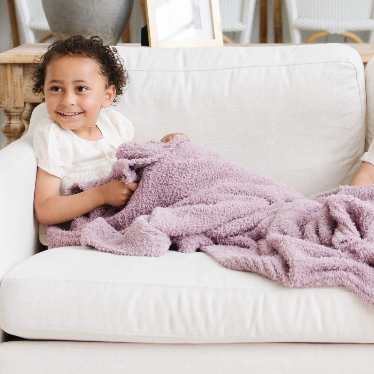Child wrapped in a pink blanket sitting on a white couch