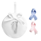 White circular ceramic baby footprint keepsake ornament with a white bow at the top, accompanied by separate blue and pink ribbon options, all on a white background.