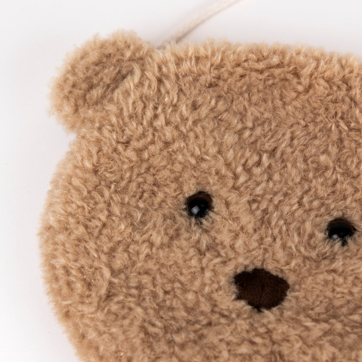 Close-up of a teddy bear face patch made from curly tan faux fur, with small black bead eyes and a dark brown stitched nose on a white background.