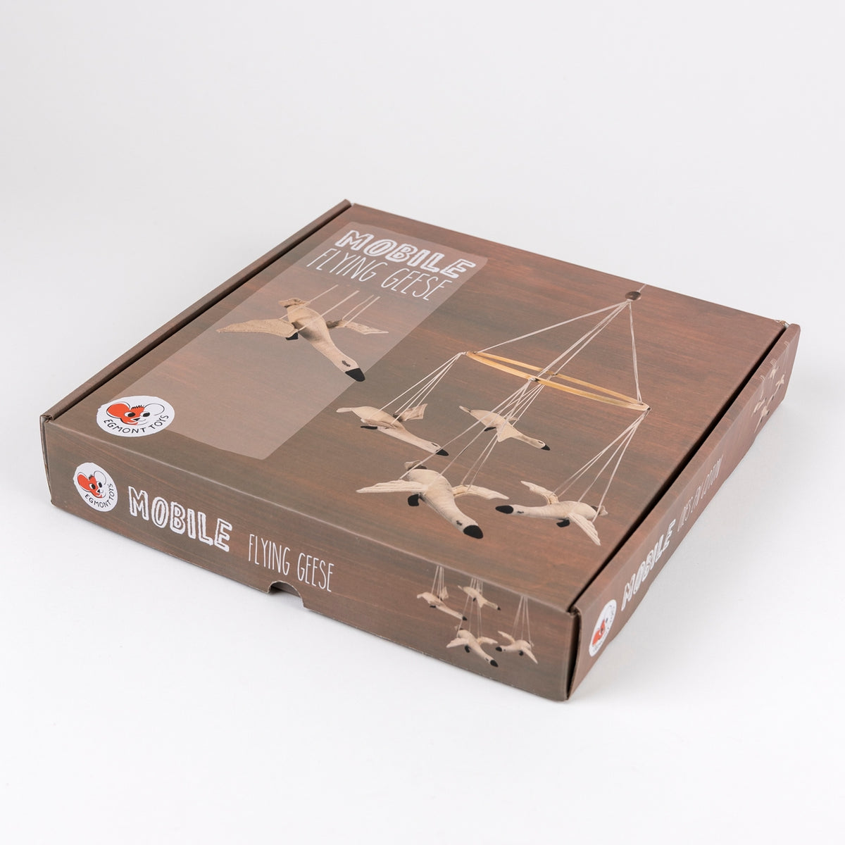 A square cardboard product box for a mobile flying geese, shown at an angle on a light gray background. The box is dark brown wood-grain textured and features printed images of light beige flying geese and a wooden hanging frame.