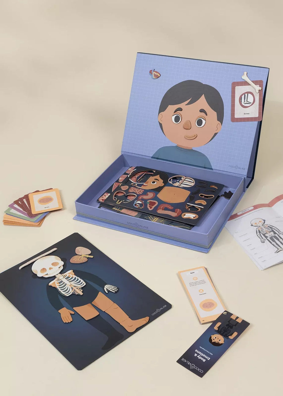 An anatomical children's educational toy set displayed on a beige background, featuring a blue illustrated storage box with a cartoon boy, a dark blue body-skeleton board, cards, and instruction sheets.