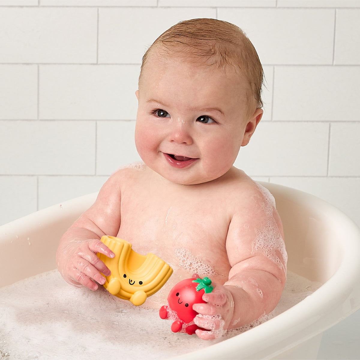 Baby in a bathtub with bath toys, smiling at the camera.