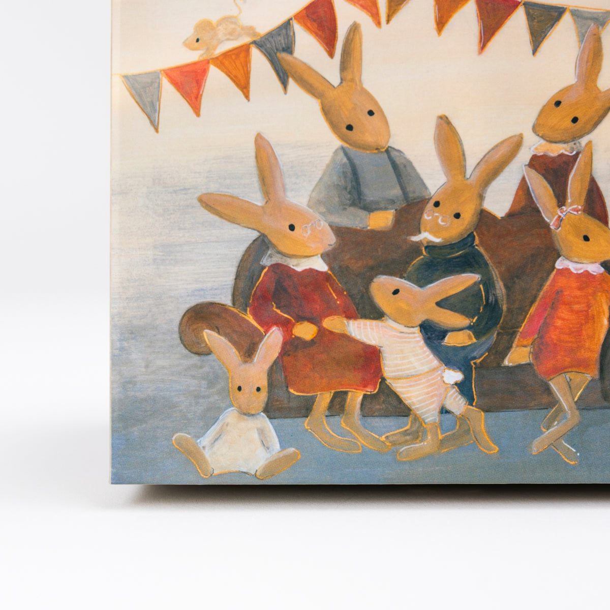 A square canvas print featuring a whimsical painting of anthropomorphic rabbits gathered around a table, decorated with bunting flags. The canvas is shown standing upright on a white surface against a light gray background.