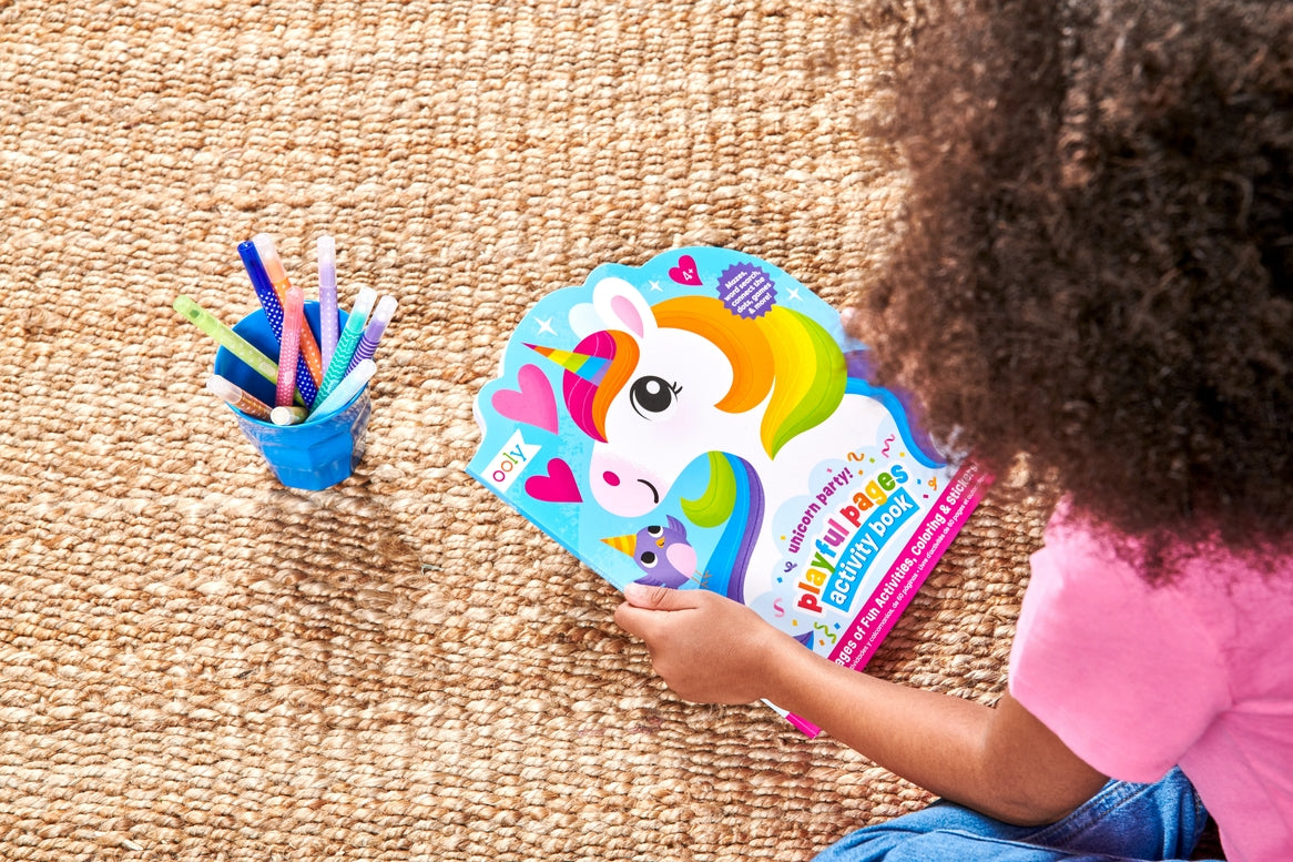 Child playing with a colorful unicorn-themed activity book on a carpeted floor.