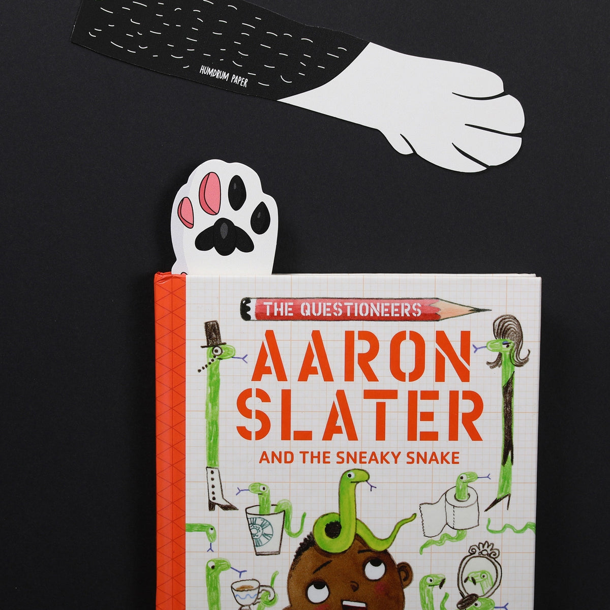 Book titled 'The Questioneers Aaron Slater and the Sneaky Snake' with paw-shaped cutouts on a black background