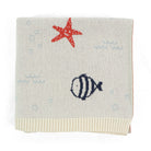 A square knit baby blanket in cream with a red starfish, a navy blue striped fish, and light blue bubble motifs, finished with a ribbed cream border.