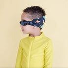 Child wearing a yellow jacket and space-themed headband on a beige background