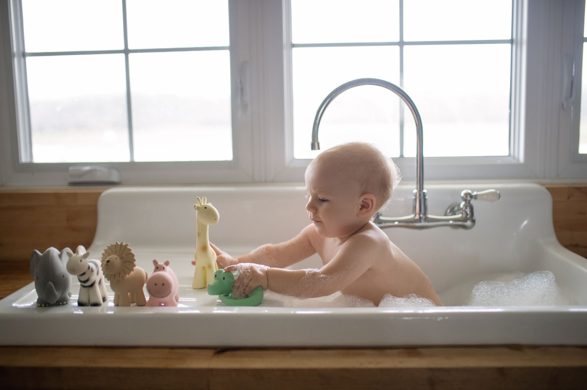 Baby playing with bath toys in a sink filled with water.
