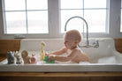 Baby playing with bath toys in a sink filled with water.