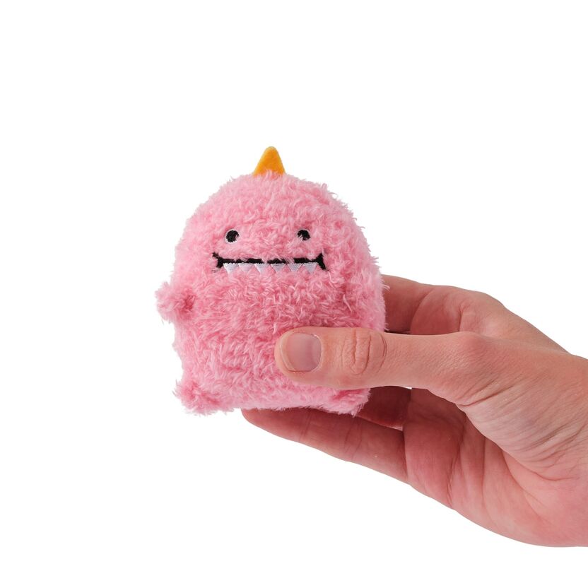 Pink plush toy with a yellow horn held in a hand against a white background