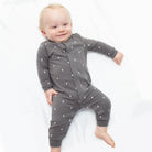 A baby lying on a white blanket wearing a dark gray long-sleeve one-piece jumpsuit with a white lightning bolt pattern.