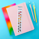 Notebook with cat-themed stickers on a blue background with colorful pens.