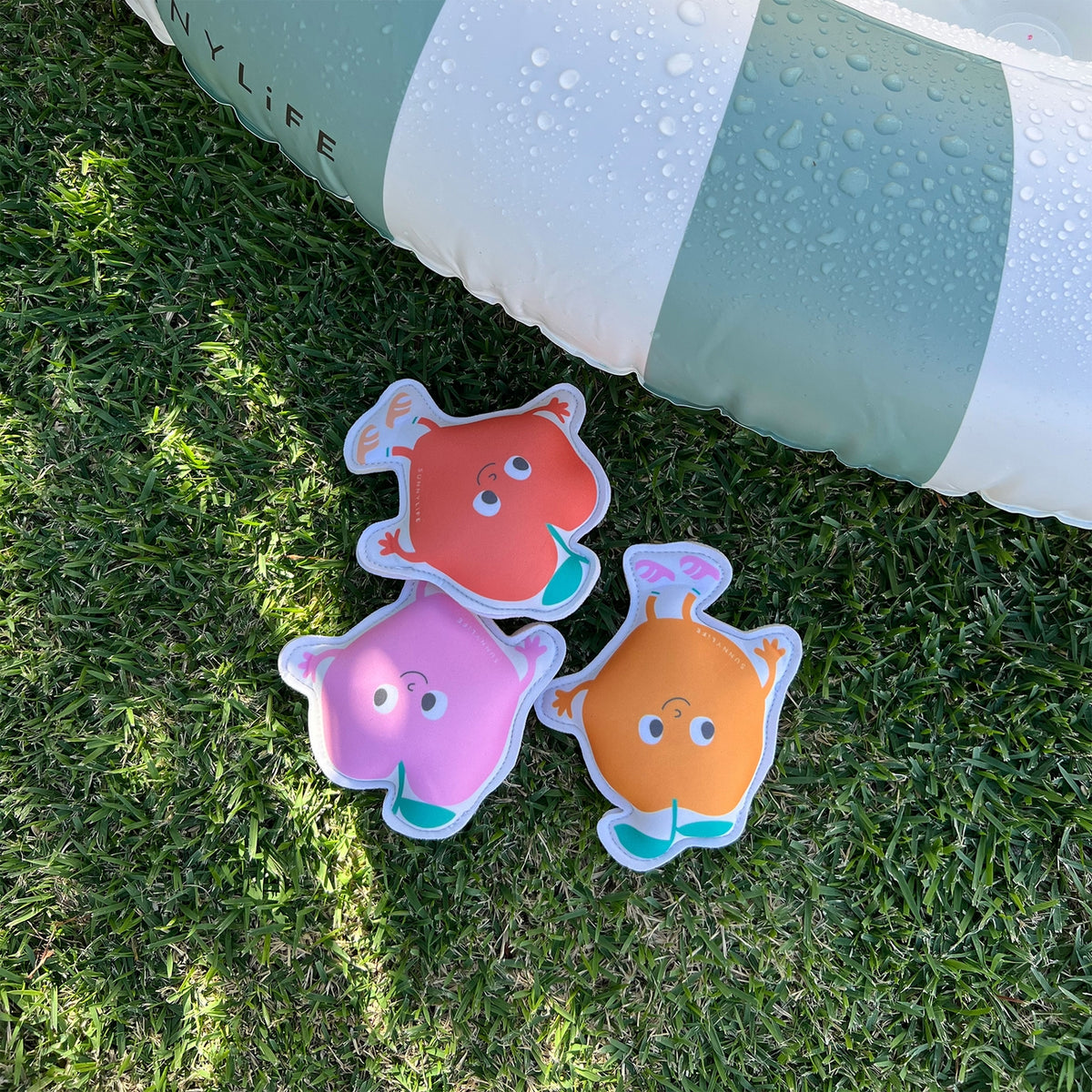 Three colorful cartoon-like stickers on grass with a pool float in the background.