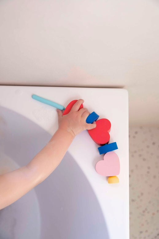 Child's hand playing with colorful heart-shaped blocks on a white surface.