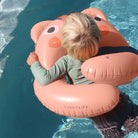 Child on a pink inflatable animal float in a pool with 'SUNNYLIFE' branding.