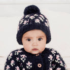 Baby wearing a dark blue knitted hat with a pom-pom and matching outfit on a light background