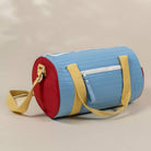 A light blue cylindrical duffel bag with red end caps, yellow straps, and a white zipper pocket, shown on a neutral beige background.