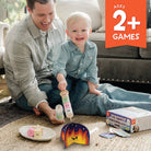 Man and child playing with toys on the floor, with a product box in the background.