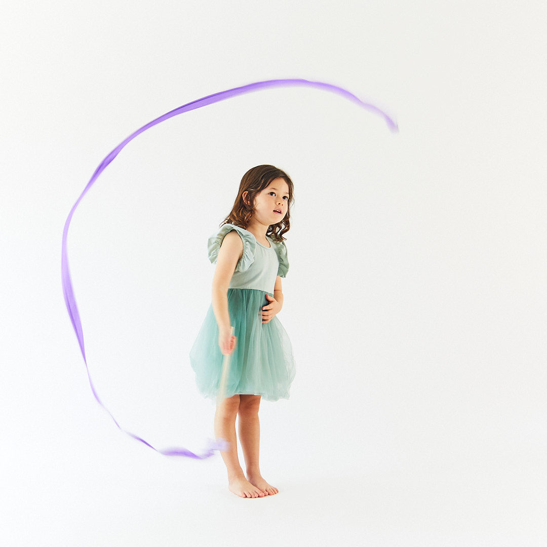 Young girl in a light green dress standing with a purple ribbon on a white background