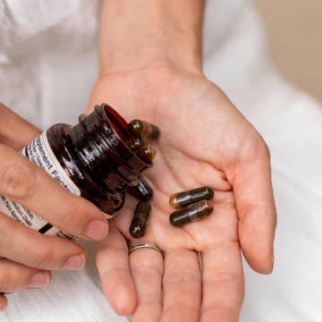 Person holding a bottle of supplements with capsules in their hand