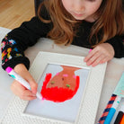 Child painting a picture of a fish with red paint on a white frame.