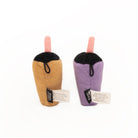Two small plush drink cup toys on a plain white background. One is tan with a pink straw and black top, and the other is lavender-purple with a pink straw and black top.