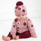 Baby wearing a pink knitted cardigan and hat with floral patterns on a white background