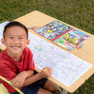 Child coloring at a table with coloring books and crayons outdoors