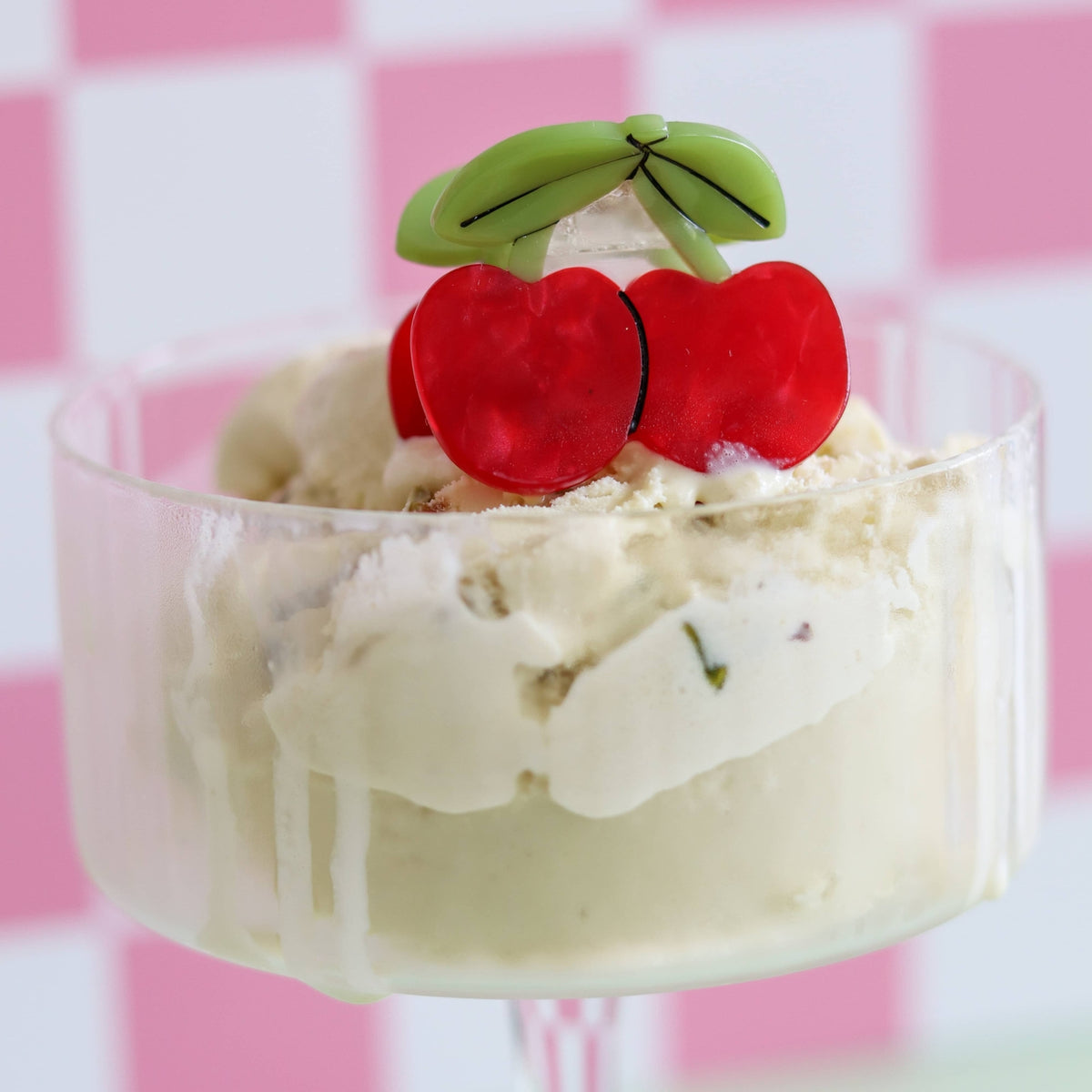 Ice cream dessert with whipped cream, cherries, and kiwi slices on a pink checkered background