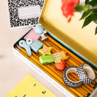 Pencil case with stationery items including pencils, scissors, and erasers on a wooden surface.