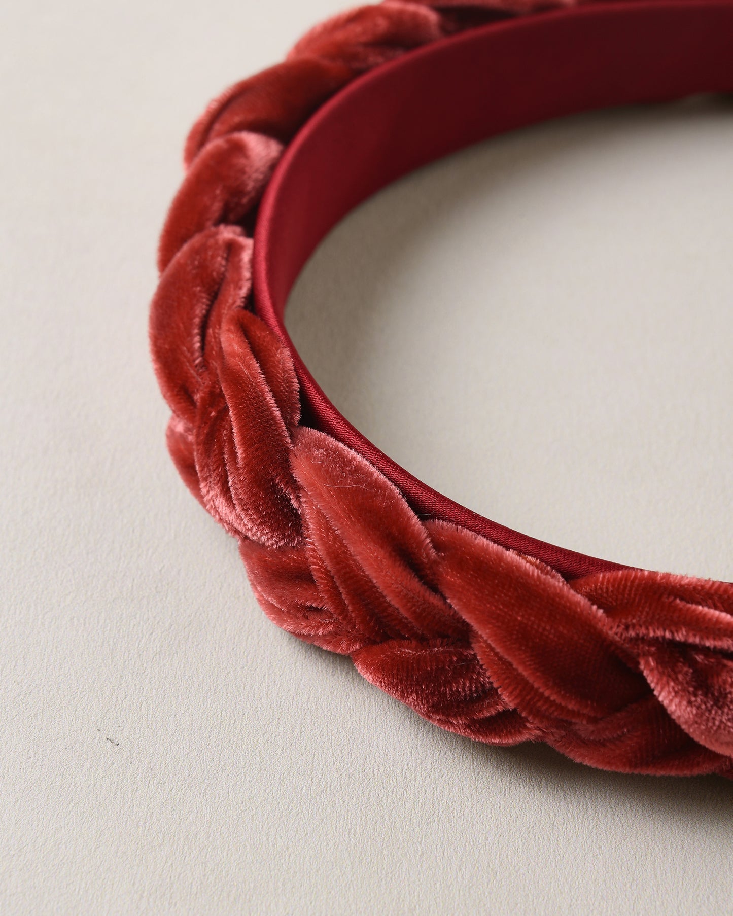 A close-up of a red velvet braided headband on a light beige textured background.