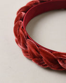 A close-up of a red velvet braided headband on a light beige textured background.