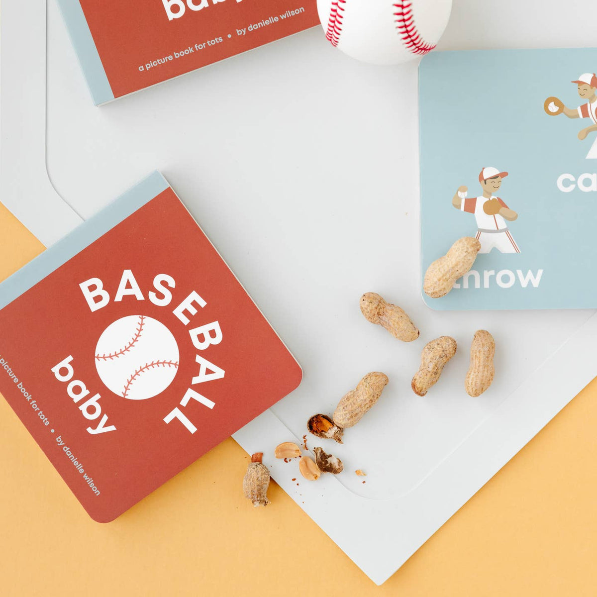 Children's books titled 'Baseball Baby' and 'Can I Throw' with peanuts on a colorful background.