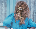 Person with curly hair wearing gold hair clips against a decorative curtain background