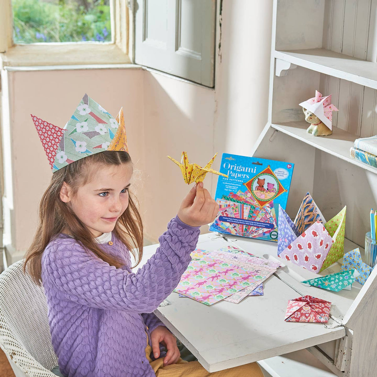 Young girl wearing a paper crown, sitting at a table with craft materials and books.