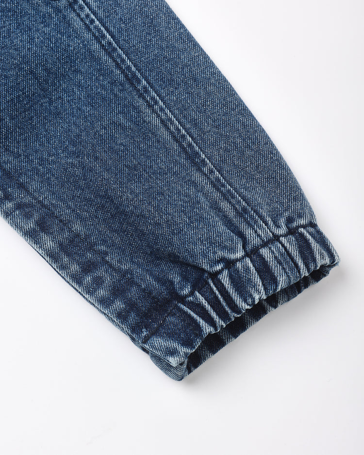 Close-up of a dark blue denim garment cuff with an elastic gathered hem, shown on a plain white background.
