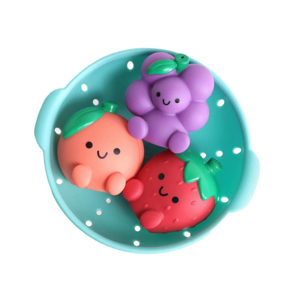 A round turquoise silicone bath toy shaped like a colander, containing three cute, smiling fruit-shaped squishy toys: a peach, a purple grape cluster, and a red strawberry.