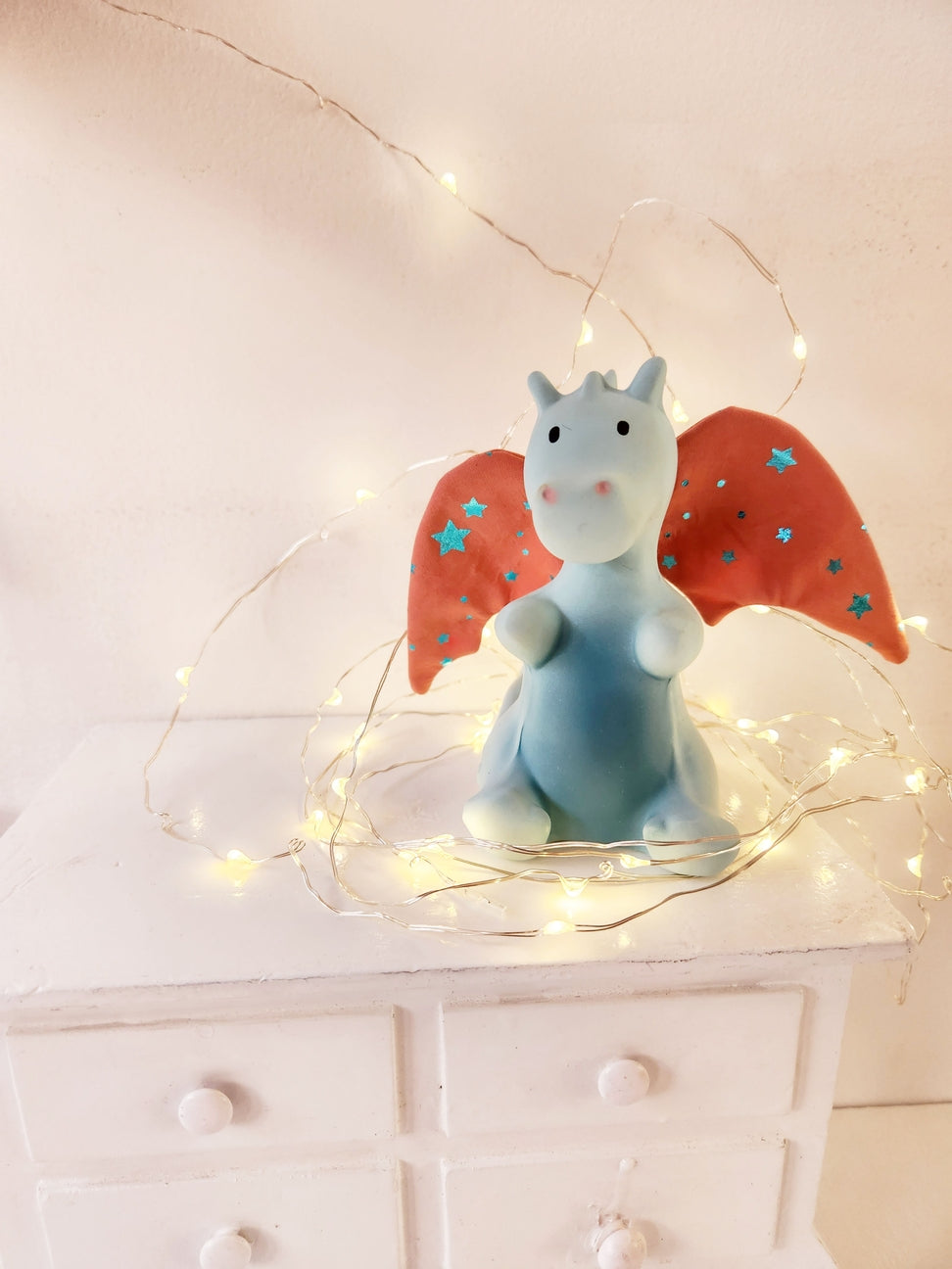Decorative figurine of a blue creature with red wings on a white surface with string lights.