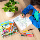 Child coloring a dinosaur picture with a coloring book and pencils on a table.