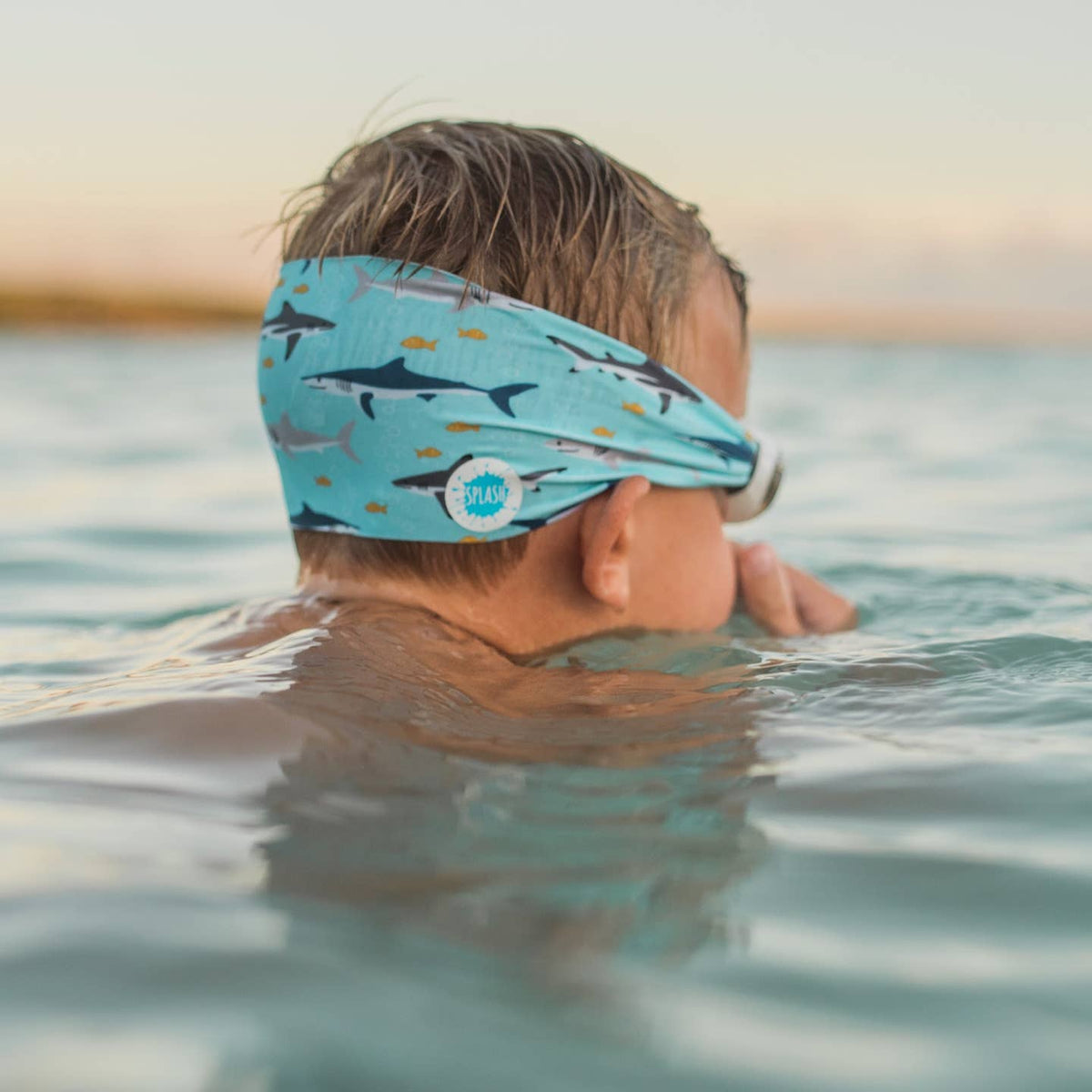 Child swimming in water wearing a blue headband with shark pattern